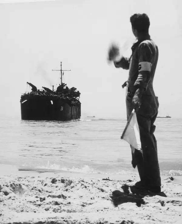 A beach-group signalman directs USS LST-314 to a Sicily beach, July–August 1943