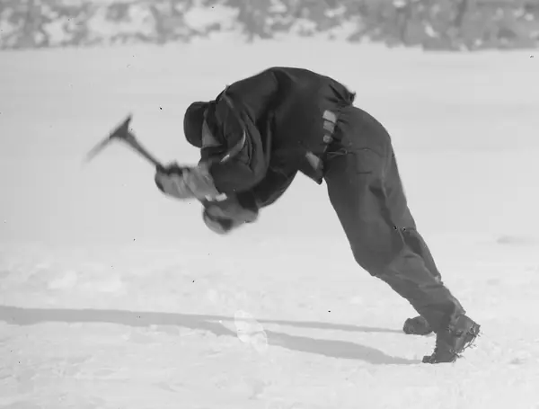 An expedition member leaning on the wind while picking ice, Cape Denison, 1912 (not Mawson)