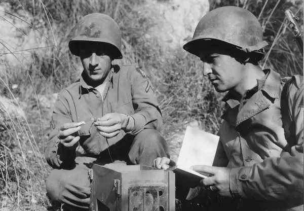 Pvt. Frank M. Mis is shown how to attach a message capsule to a pigeon’s leg by Pfc. John A. Oeverso, 45th Division command post, Italy, December 18, 1943 (not G.I. Joe)