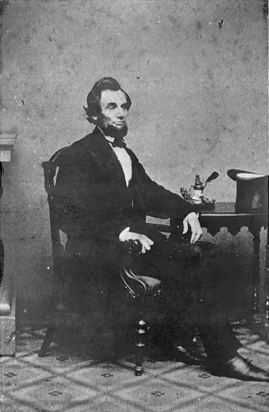 Full length portrait of Lincoln seated next to a small table, 24 Feb. 1861