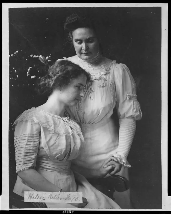 Helen Keller, three-quarter length, seated, facing right; holding hand of her teacher, Mrs. John A. Macy (Anne Mansfield Sullivan) LCCN2002706661