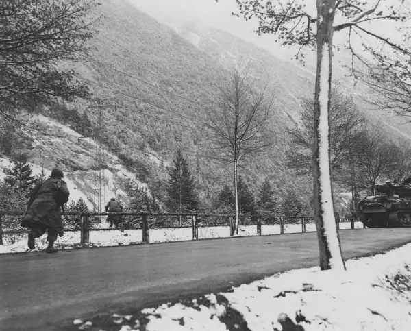 Infantrymen of the 103rd Infantry Division advance across a road and over a fence, May 1, 1945 (not Medicine Crow)