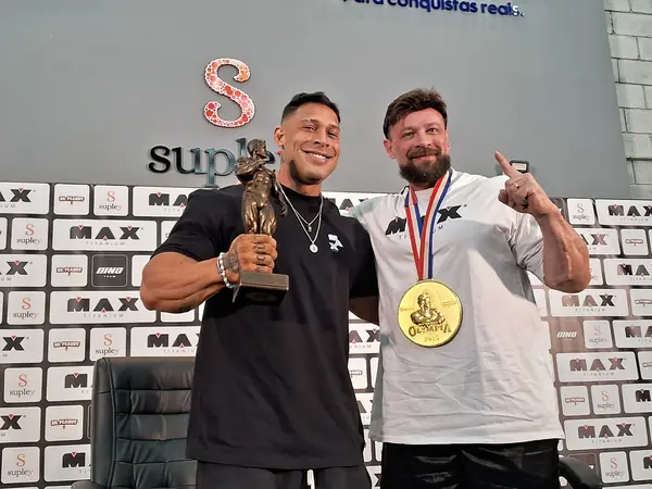 Ramon Dino with the trophy beside his coach, Fabrício Pacholok, who wears the 2025 Olympia medal, Brazil, October 16, 2025